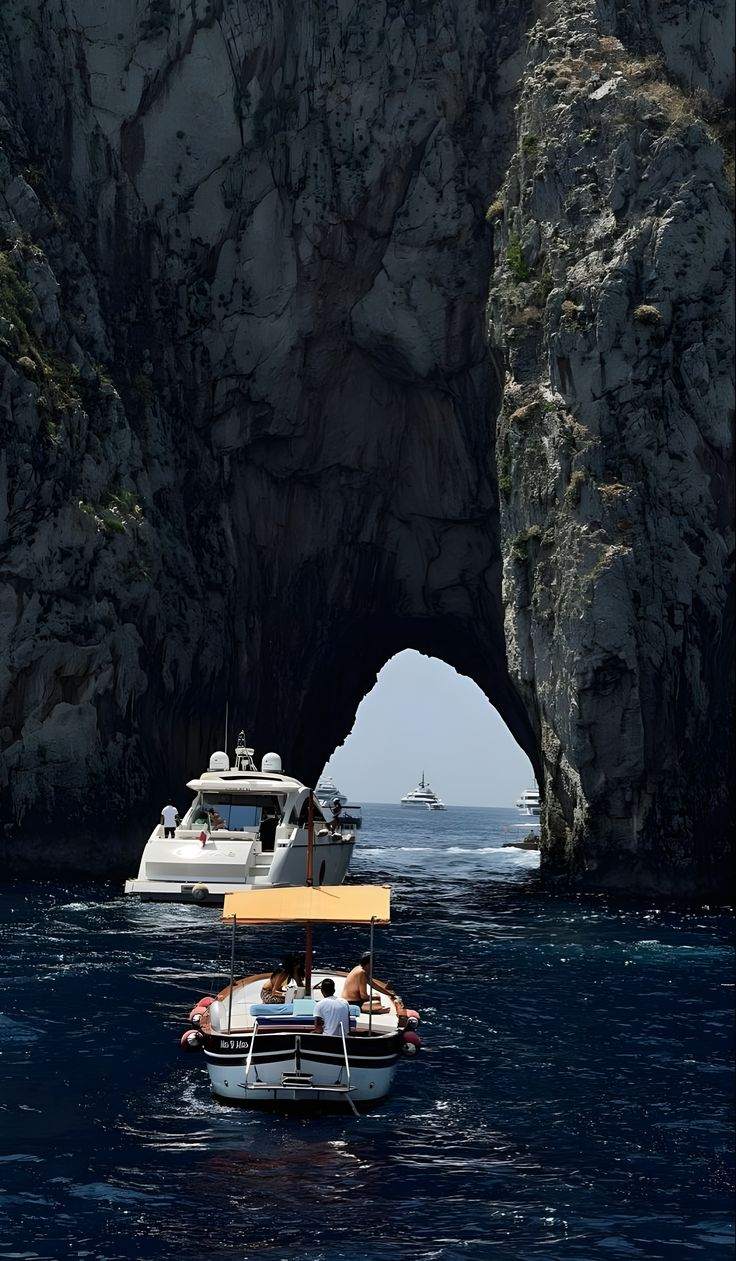 Una barca passa sotto l'arco dei Faraglioni di Capri