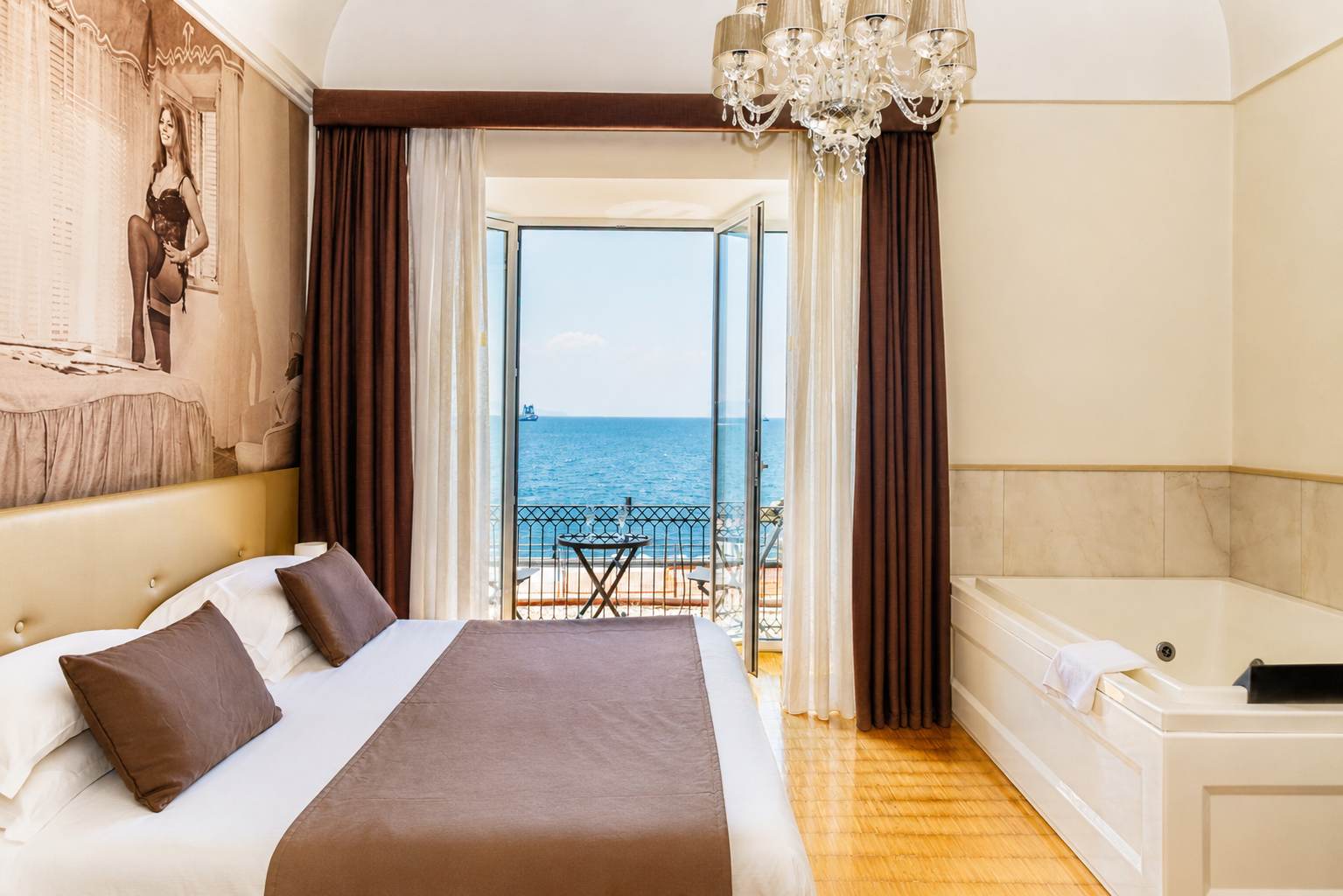 La Suite Sophia aperta sul balcone: il letto, la vasca idromassaggio e il mare del golfo